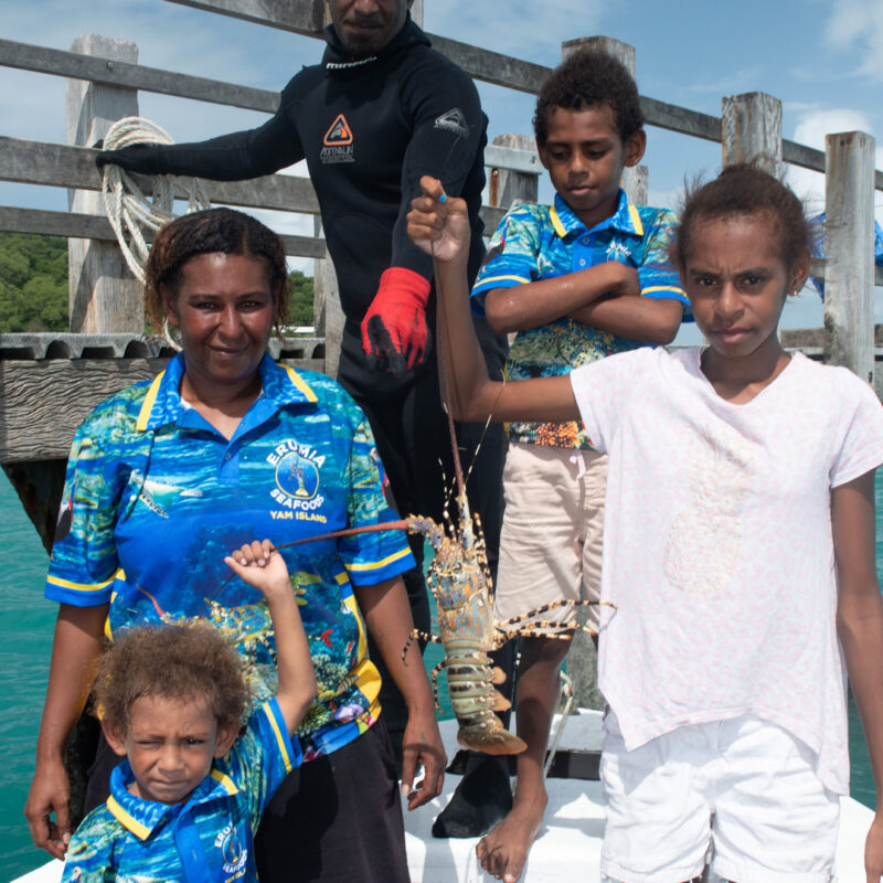 Torres Strait Islander family on Yam Island proudly holding a freshly caught tropical rock lobster, part of MG Kailis sustainable seafood operations in Northern Australia